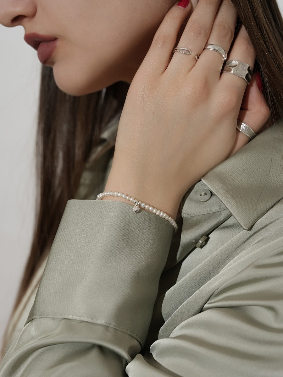 Strieborný náramok zdobený pravými sladkovodnými perlami a príveskom v tvare srdca na ruke